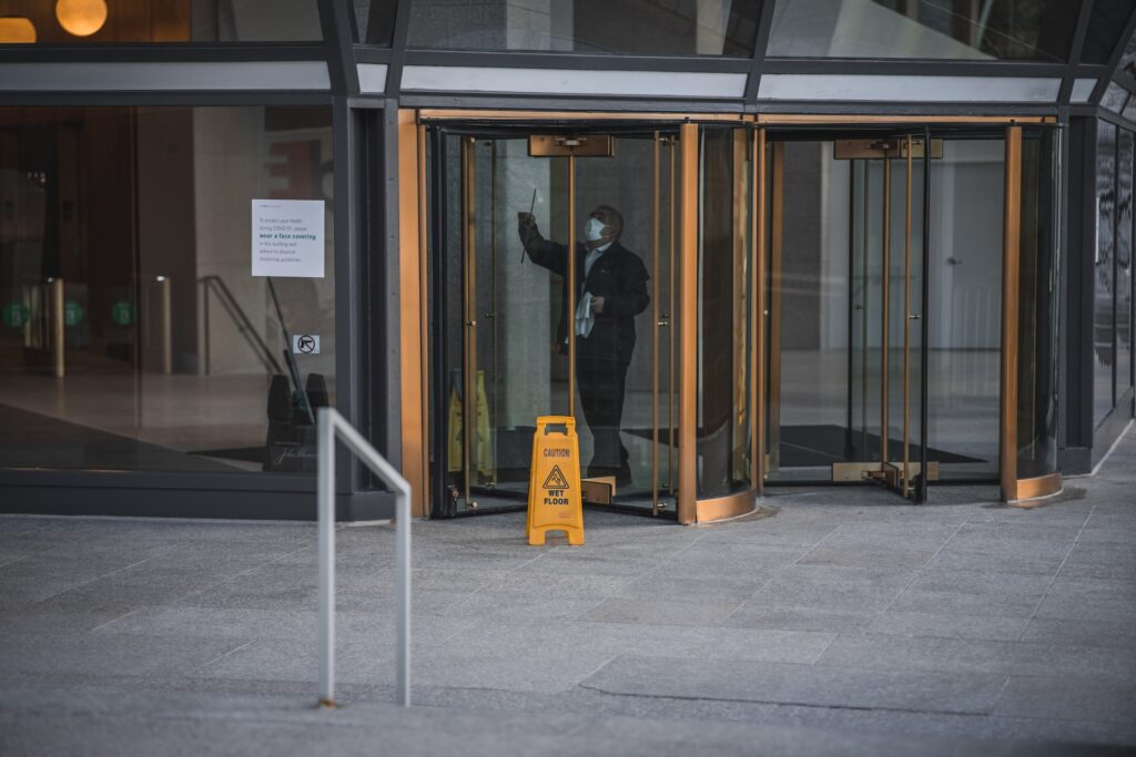 Person cleaning glass revolving doors of a commercial building in a city.