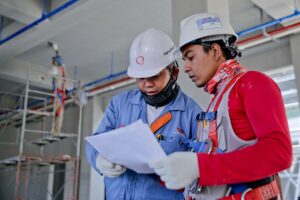 Two construction workers on-site, standing together consulting a paper.