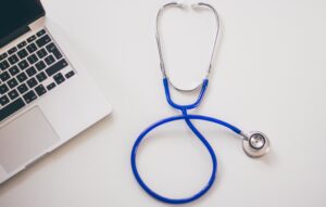 Blue stethoscope next to laptop on a white surface.