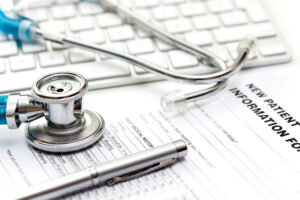 Close-up of blue stethoscope on top of patient information form, in front of white keyboard.