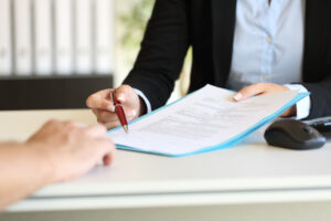a business person's hands holding a pen and indicating where to sign a contract at office