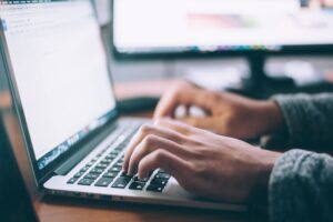 Hands typing on a silver laptop.